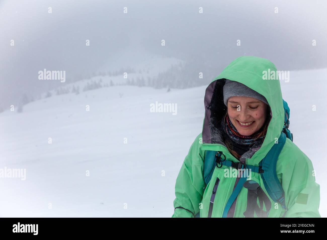 Les flocons de neige dansent dans les airs tandis qu'un passionné de plein air rayonne de joie, leur veste imperméable de couleur citron se démarque des paysages hivernaux blancs Banque D'Images