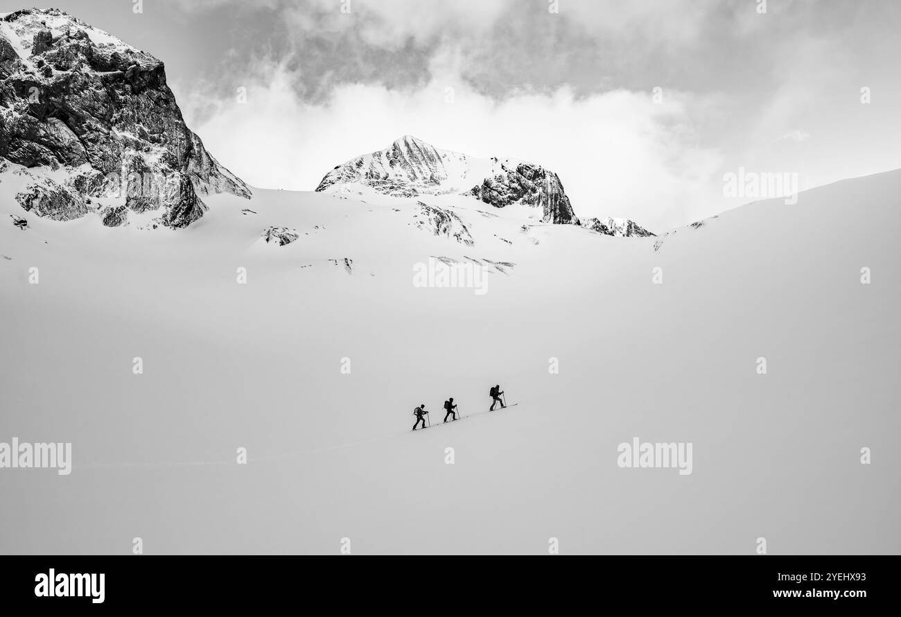 Trois randonneurs de ski dans un paysage solitaire, paysage de montagne enneigé, photo noir et blanc, ambiance nuageuse, haute randonnée, Alpes bernoises, Oberlan bernois Banque D'Images