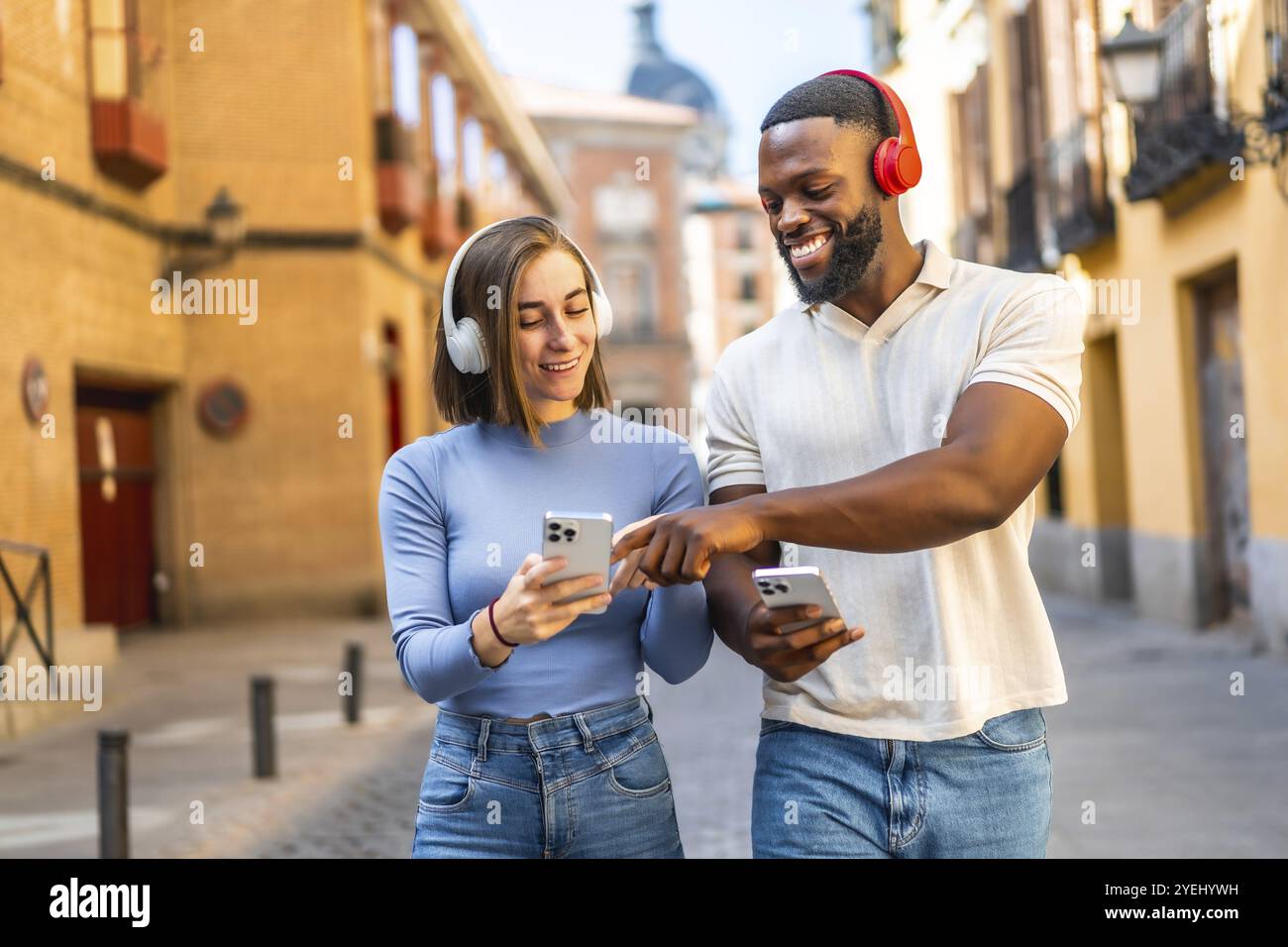 Heureux couple multi-ethnique écoutant de la musique et utilisant le téléphone portable marchant dans la ville Banque D'Images