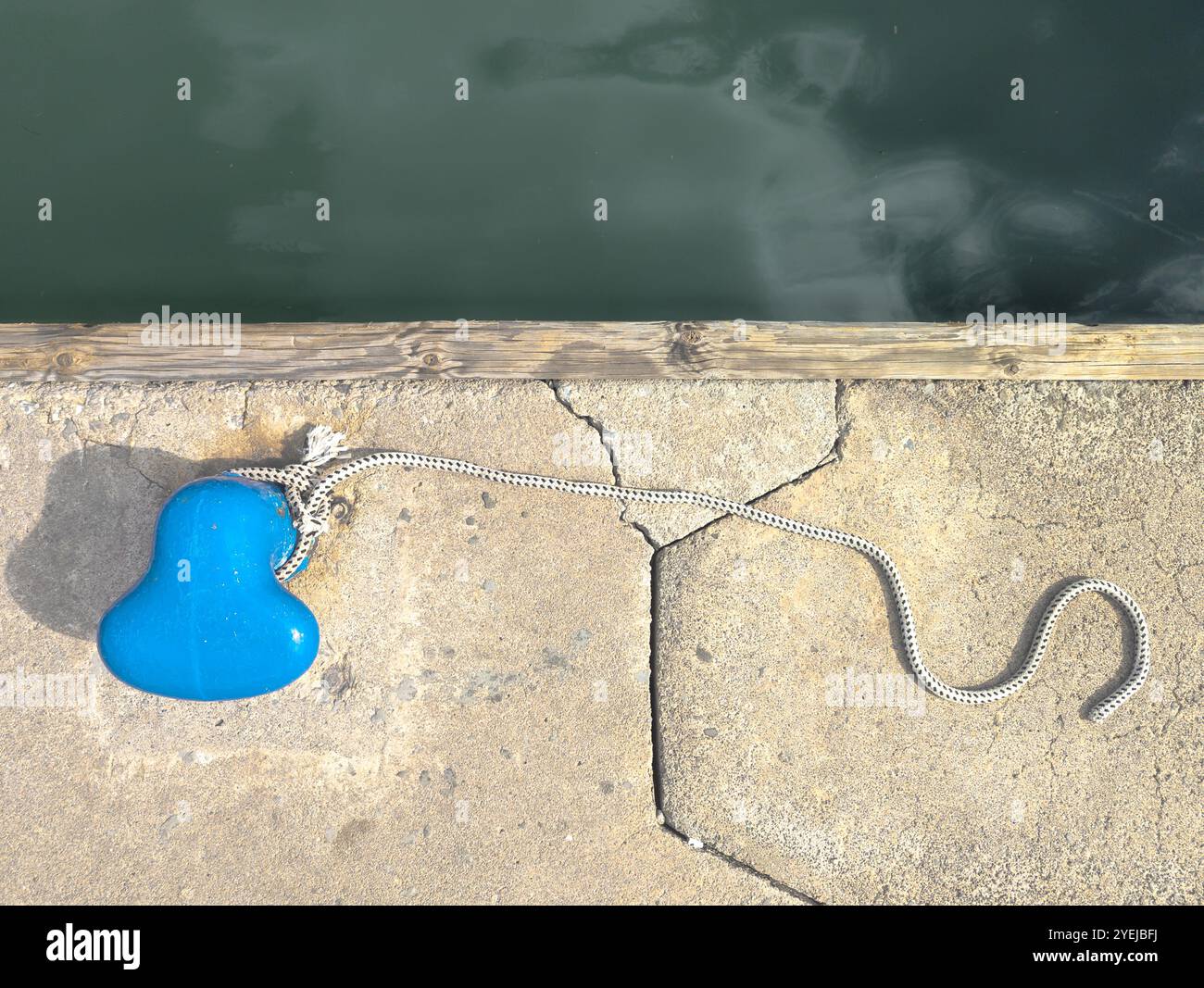 Une photo de haut en bas d'une borne bleu vif en bord de mer et d'une corde utilisée pour attacher de petits bateaux photographiés par une journée ensoleillée et brillante Banque D'Images
