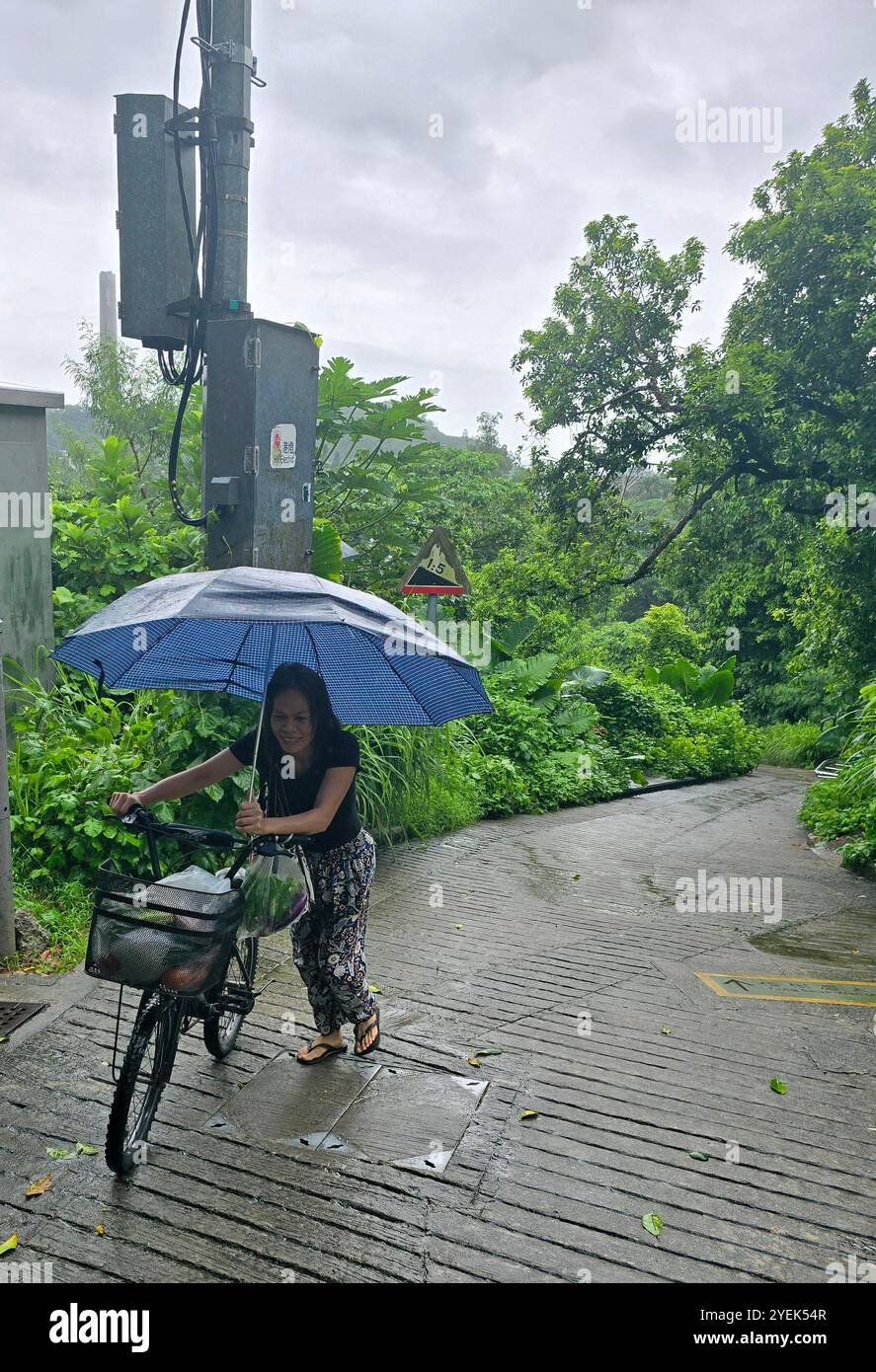 Une femme poussant son vélo sur la colline un jour de pluie. Lamma Island, Hong Kong. - Image de stock capturée avec un smartphone