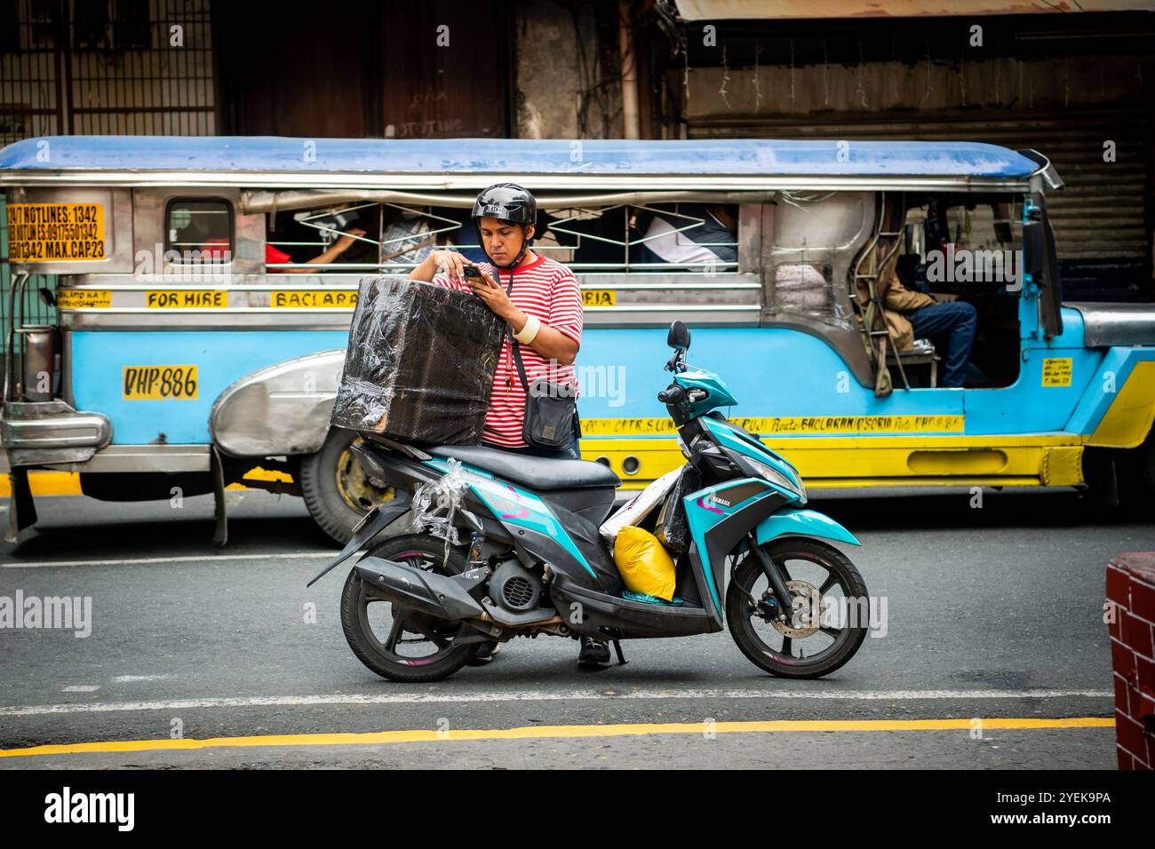 Un philippin emballe son étui de vélo alors que les jeepneys passent à vitesse. Dans le quartier Ermita de la ville de Manille, Philippines. Banque D'Images