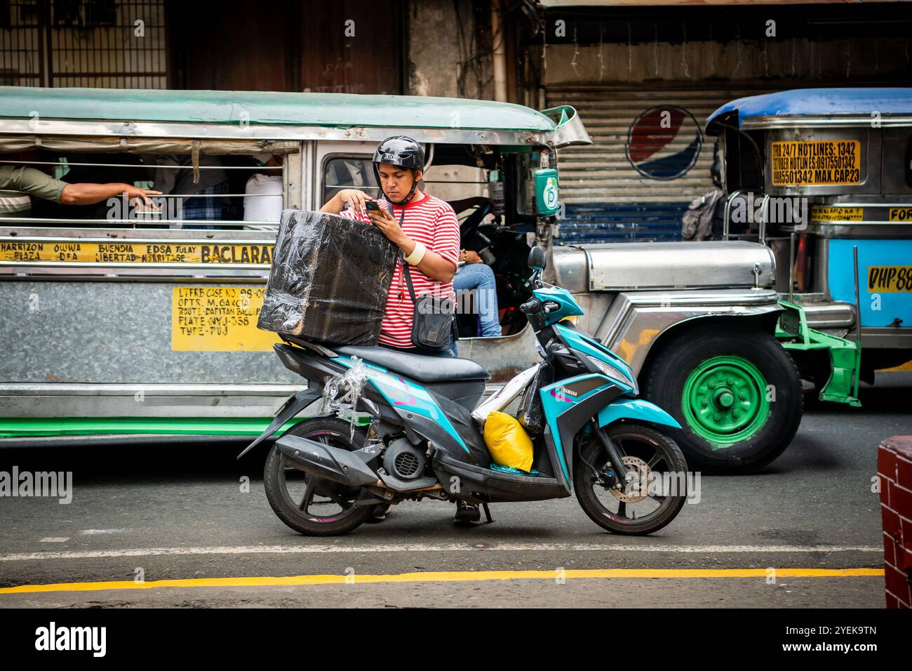 Un philippin emballe son étui de vélo alors que les jeepneys passent à vitesse. Dans le quartier Ermita de la ville de Manille, Philippines. Banque D'Images