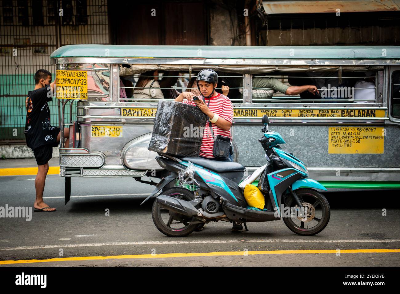 Un philippin emballe son étui de vélo alors que les jeepneys passent à vitesse. Dans le quartier Ermita de la ville de Manille, Philippines. Banque D'Images
