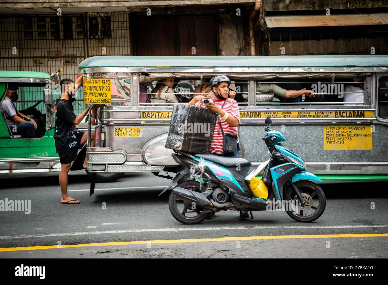 Un philippin emballe son étui de vélo alors que les jeepneys passent à vitesse. Dans le quartier Ermita de la ville de Manille, Philippines. Banque D'Images