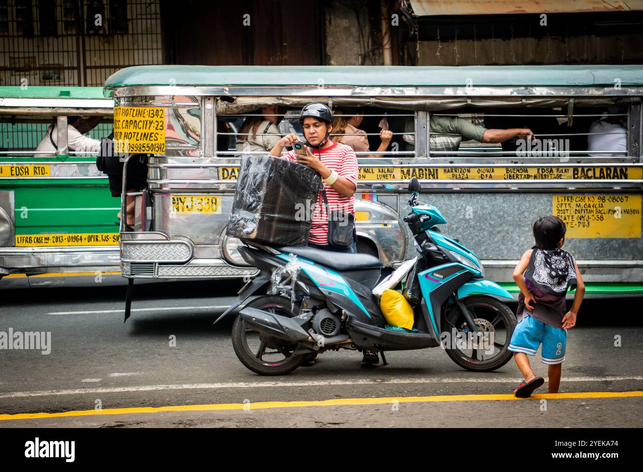 Un philippin emballe son étui de vélo alors que les jeepneys passent à vitesse. Dans le quartier Ermita de la ville de Manille, Philippines. Banque D'Images