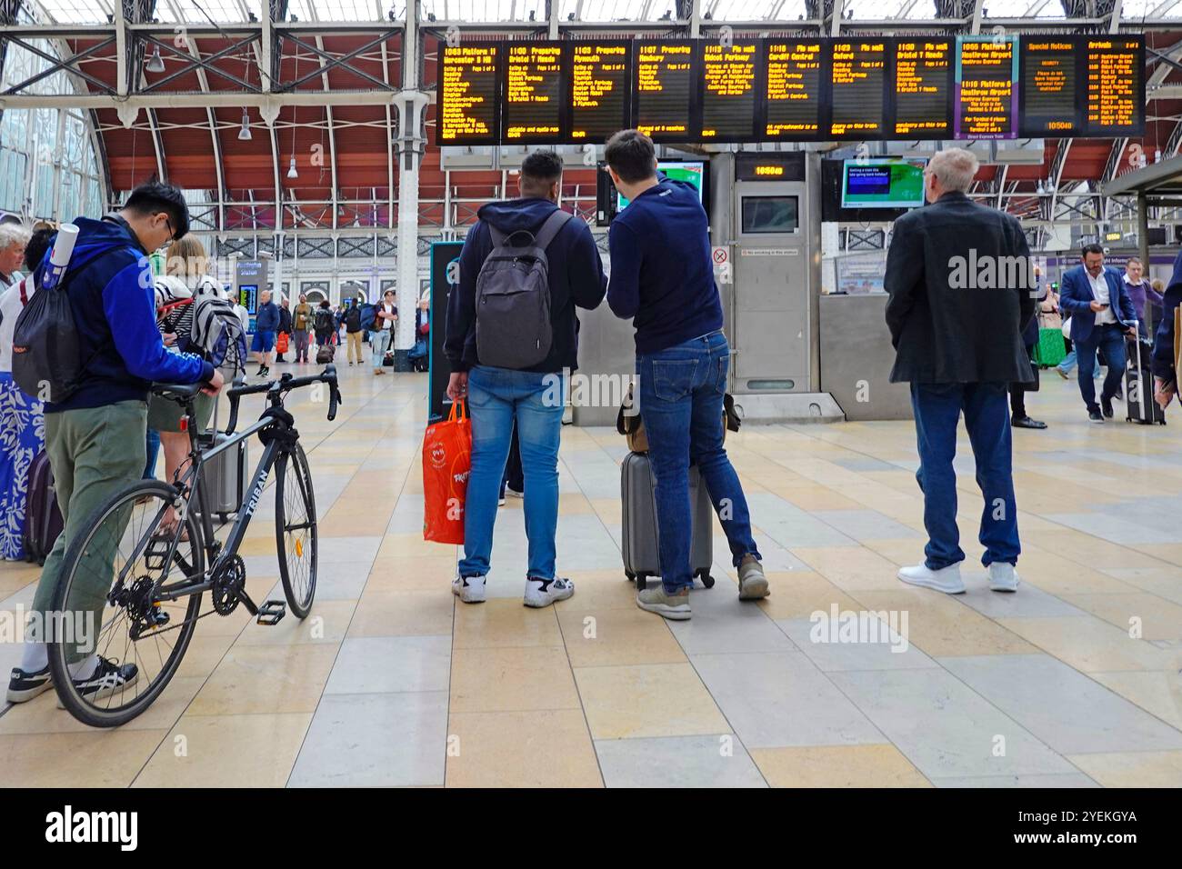 Vue arrière de la gare de Paddington des voyageurs masculins vérifiant les heures de départ sur les grands panneaux de destination avec cycliste tenant le vélo Londres Angleterre Royaume-Uni Banque D'Images