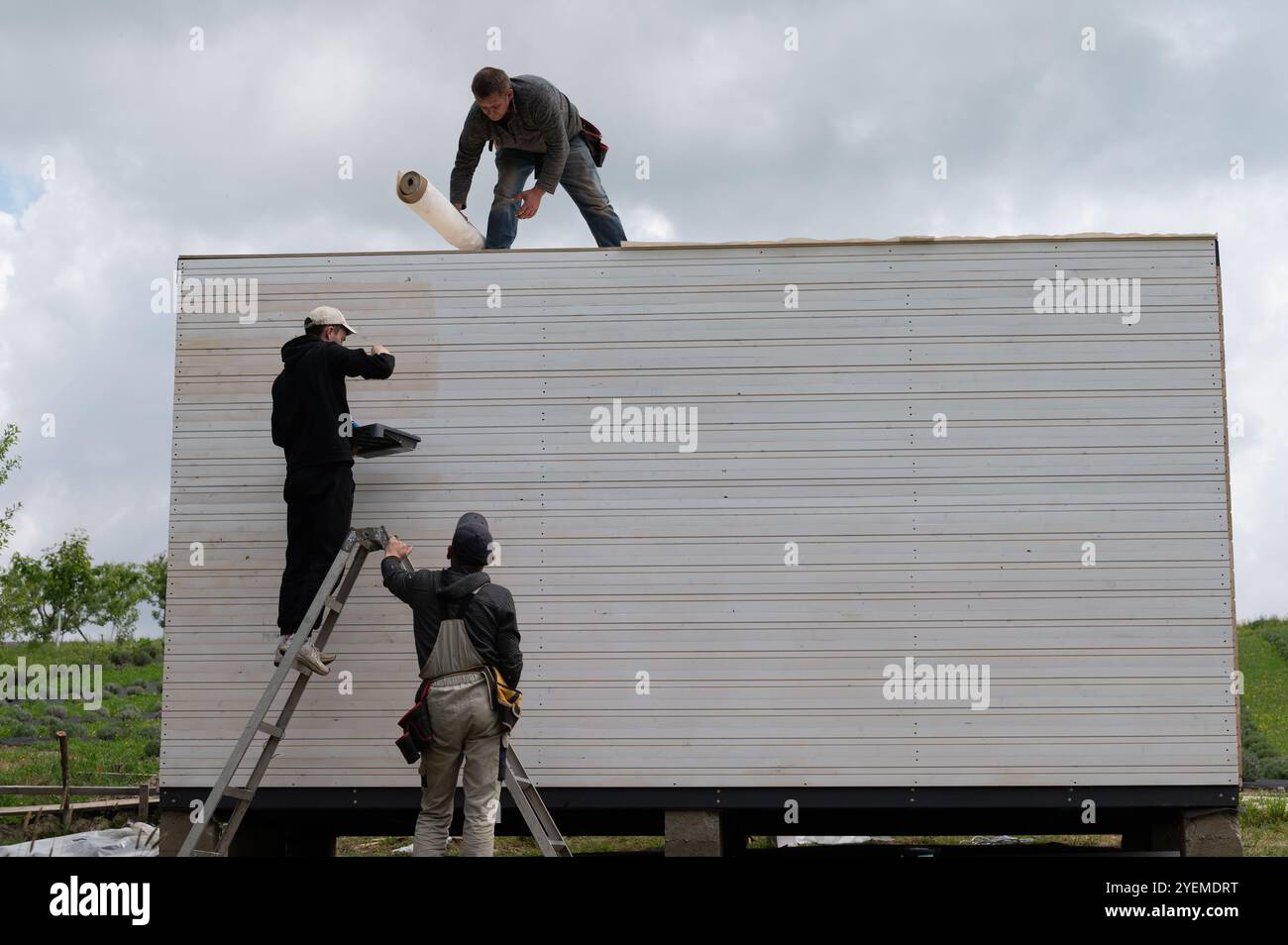 Ivano-Frankivsk, Ukraine, 11 mai 2024 : un gars peint le mur du gazebo blanc, le deuxième homme traite du toit du gazebo, travail d'assemblage avec esprit Banque D'Images