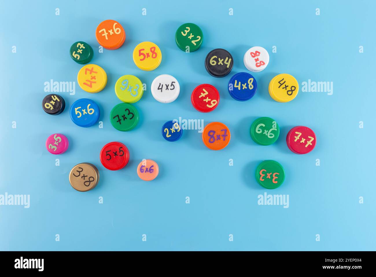 bouchons de bouteille colorés avec des problèmes de multiplication sur fond bleu. Concept éducatif à plat. jeu de mémorisation de table de multiplication, effectiv Banque D'Images