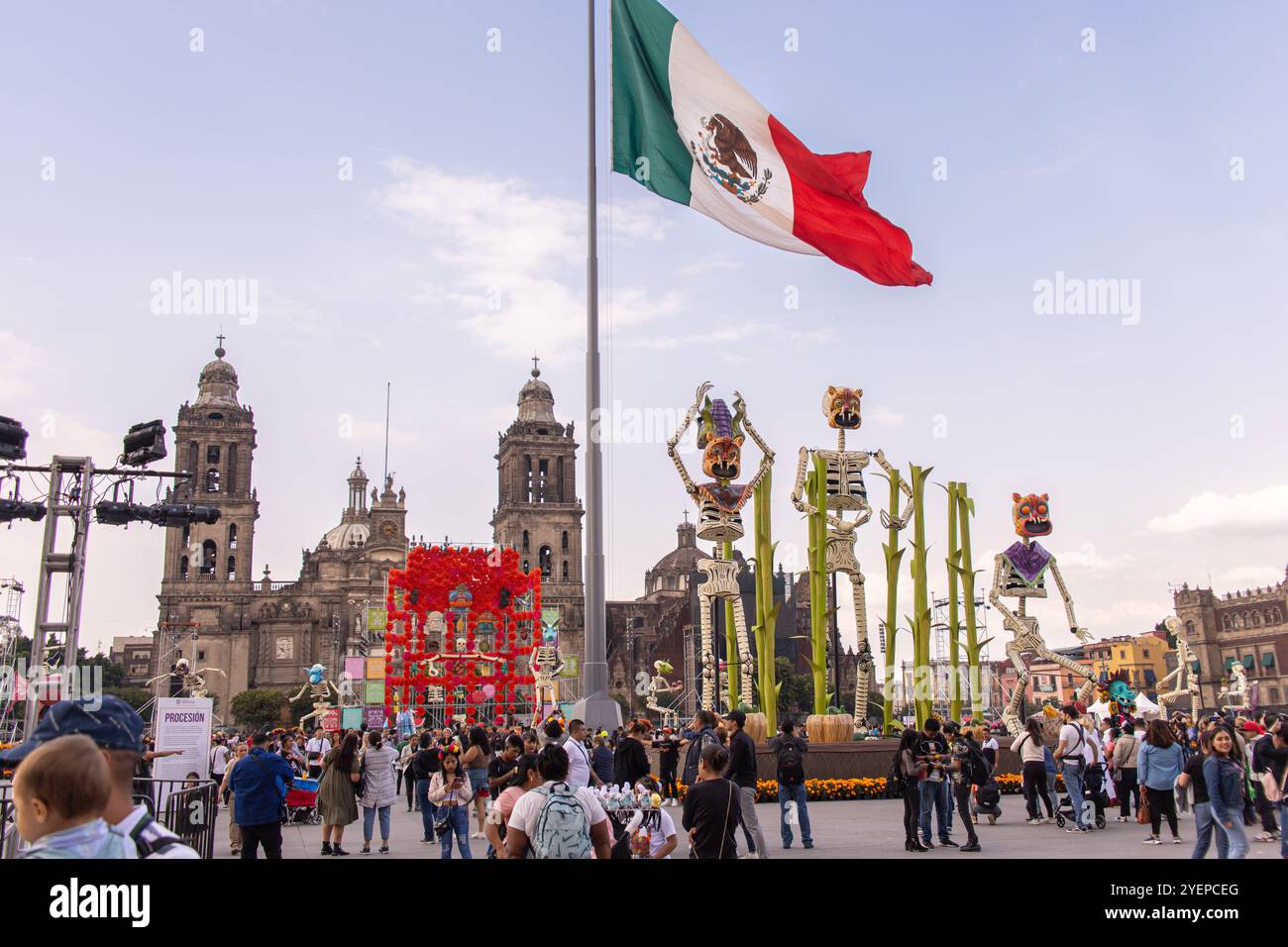 Un grand drapeau mexicain flotte au-dessus de Zócalo, entouré de décorations du jour des morts (Dia de Muertos) et de foules célébrant la fête. Banque D'Images