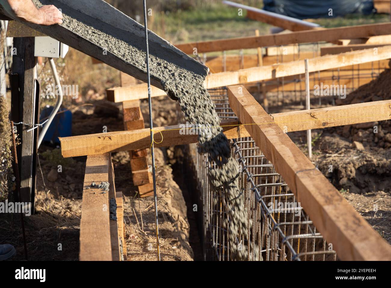 Un travailleur de la construction verse du béton d'un malaxeur de béton dans les fondations d'une maison sur un chantier de construction Banque D'Images