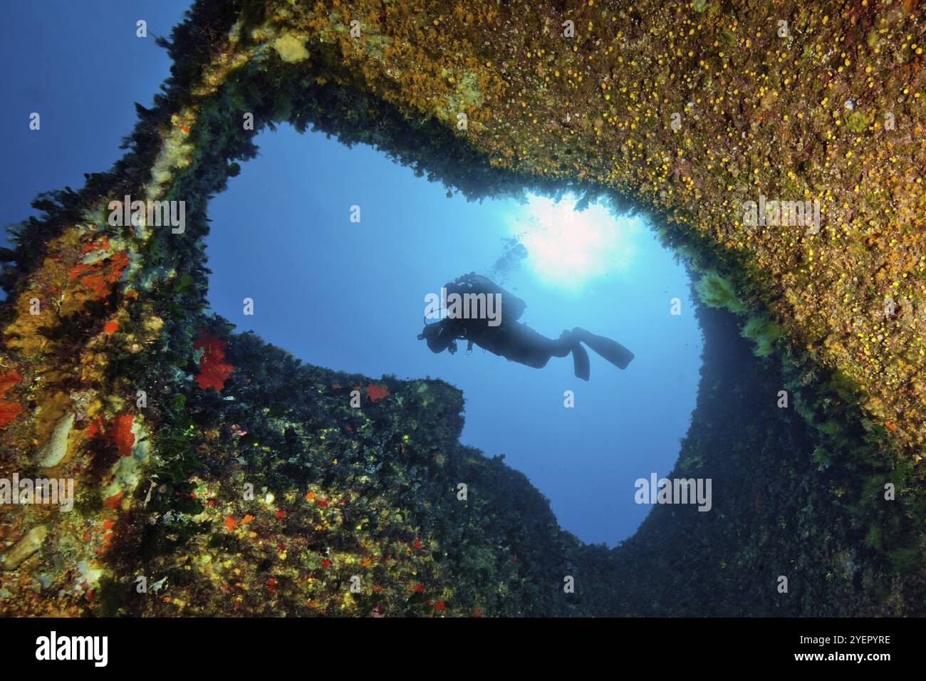 Photo sous-marine avec vue à travers une petite percée de tunnel dans le récif rocheux sur plongeur plongeur en contre-jour dans le soleil de fond sur la surface de la mer, Medi Banque D'Images