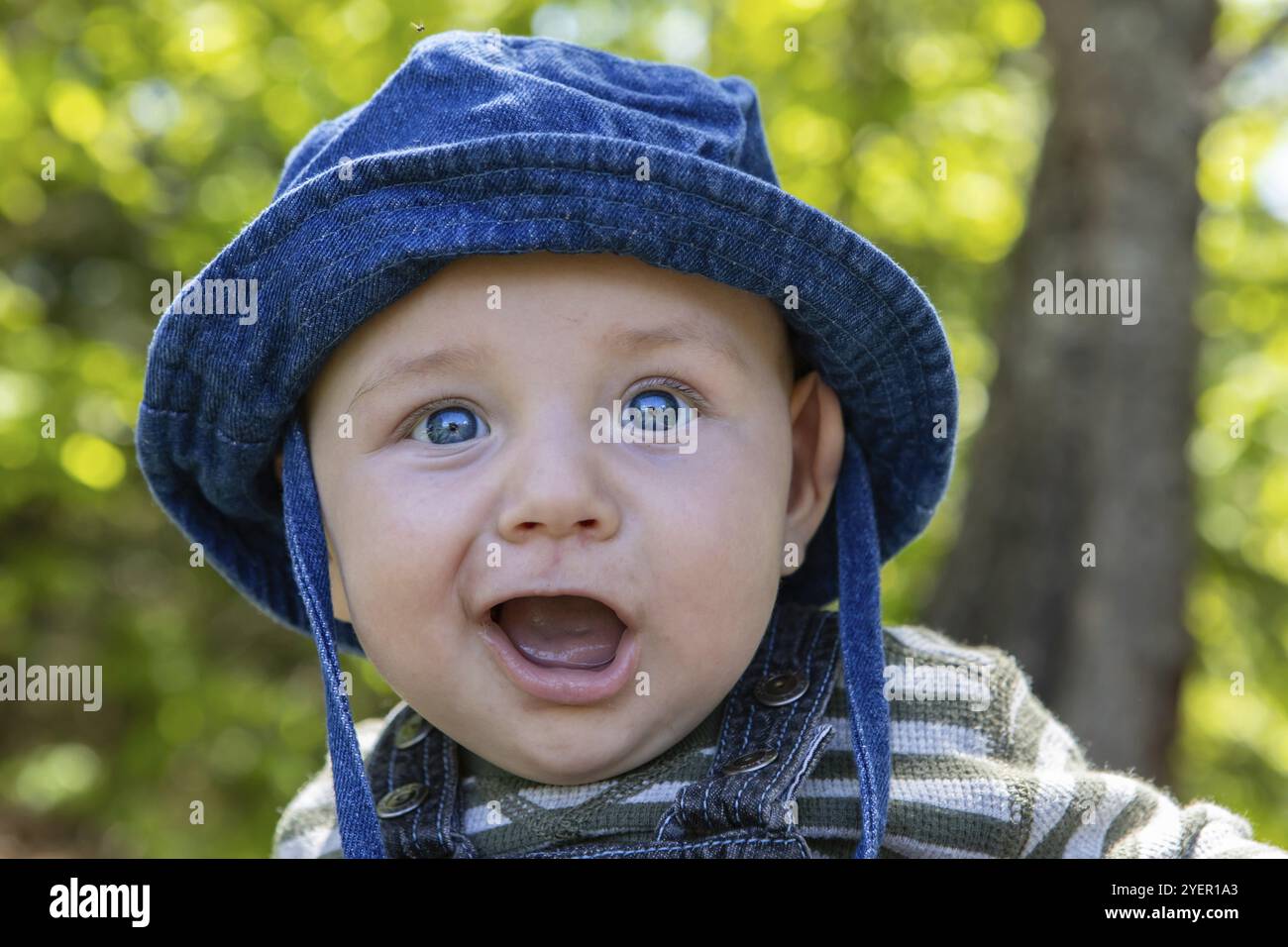 Portrait d'un petit bébé mignon avec les yeux bleus chapeau assis dans le parc avec la bouche large ouvert en appréciant et en se relaxant à l'extérieur jardin Banque D'Images