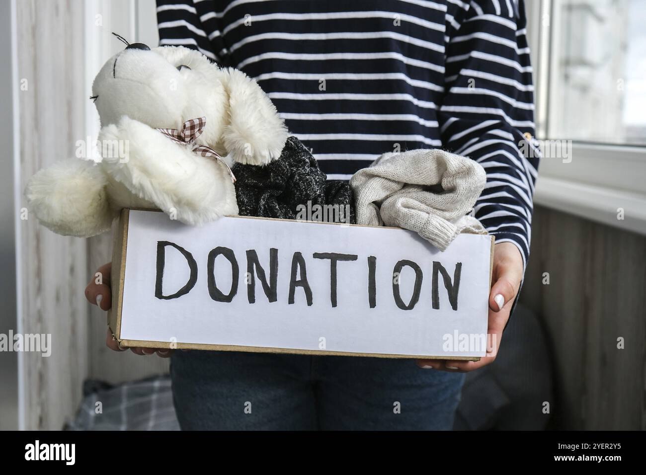 Une femme volontaire tient une boîte de dons avec des jouets et des vêtements usagés à l'intérieur.Bonne charité.Femme méconnaissable tenant une boîte avec des vêtements. clos Banque D'Images
