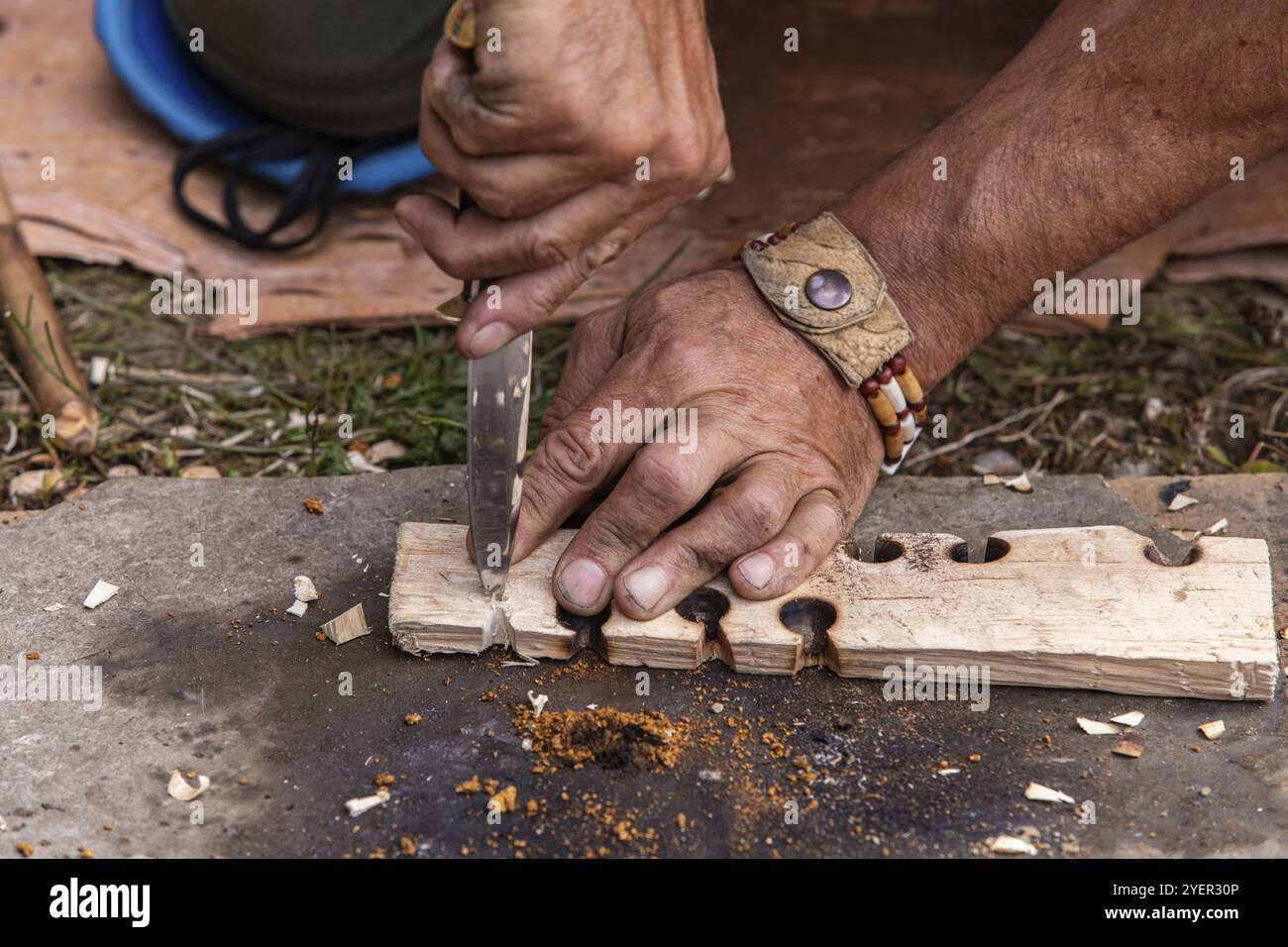 Main de l'homme tenant le couteau tout en donnant la démonstration de feu léger sur la dalle de bois avec des trous brûlés en utilisant la technique traditionnelle native au festival mondial Banque D'Images