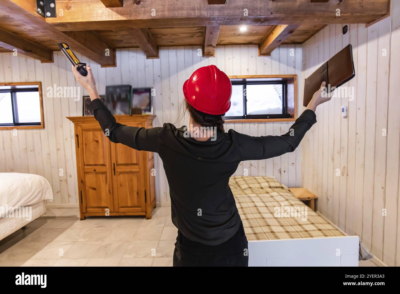 Vue arrière d'une femme inspecteur de construction portant un casque de sécurité rouge, elle lève les mains en tenant une planche à pince et un niveau à bulle Banque D'Images
