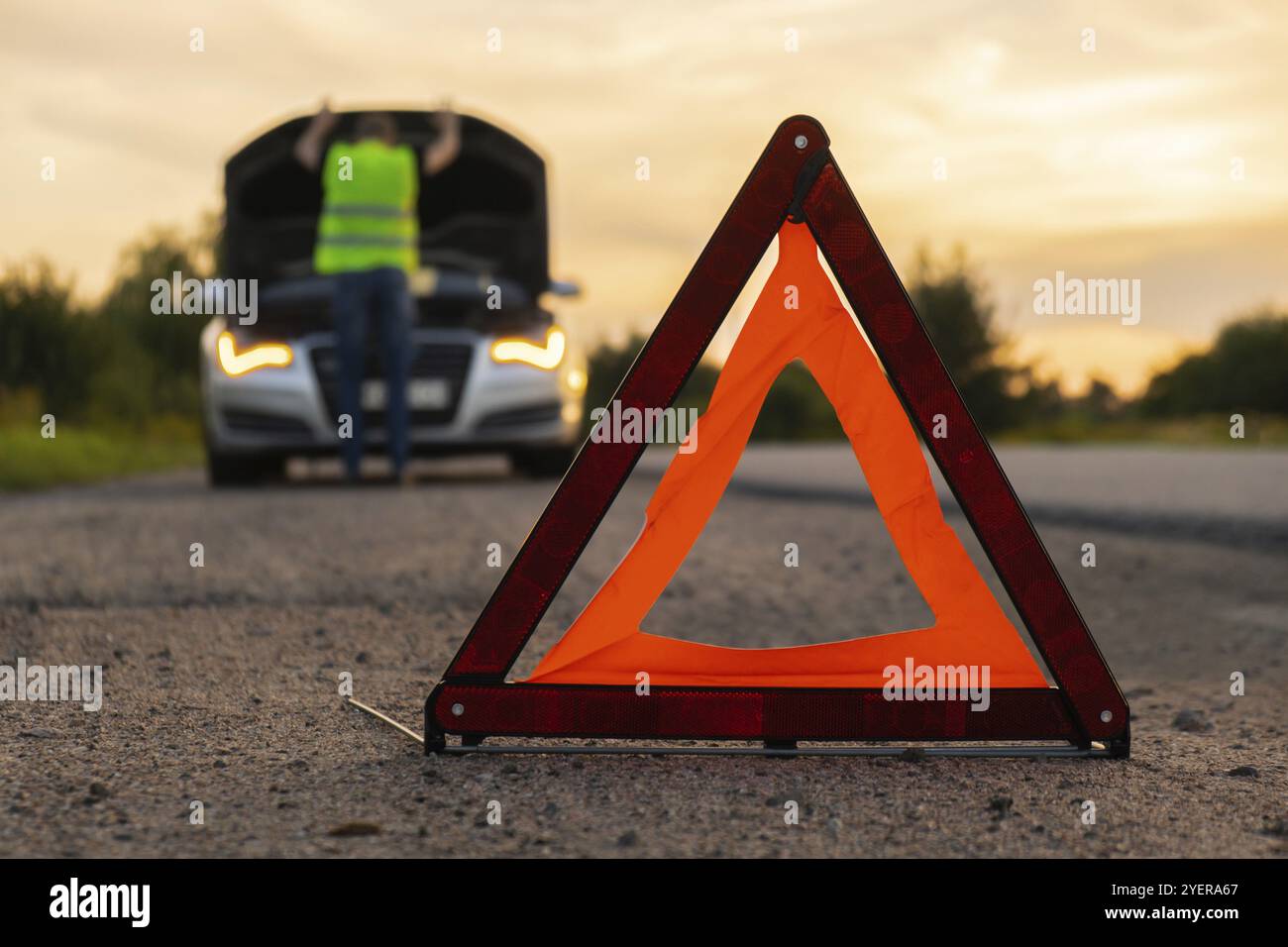 Accident d'urgence d'une voiture de luxe en argent cassé. Conducteur homme installant le panneau d'arrêt triangle rouge sur la route. Automobile de sport allumée des clignotants technique probl Banque D'Images