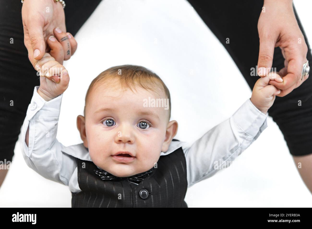 Portrait d'un nouveau-né debout avec un support de main parent porté vêtements formels posant pour photoshoot sur fond blanc Banque D'Images