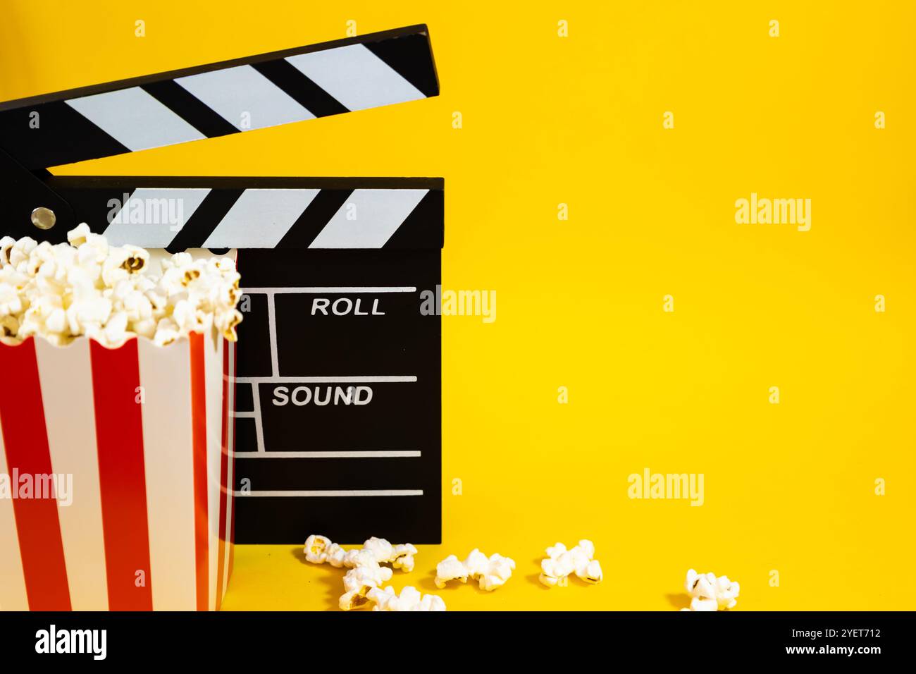 Image horizontale de pop-corn avec clapet en bois sur un fond jaune avec pop-corn dispersé autour, cinéma et concept de divertissement Banque D'Images