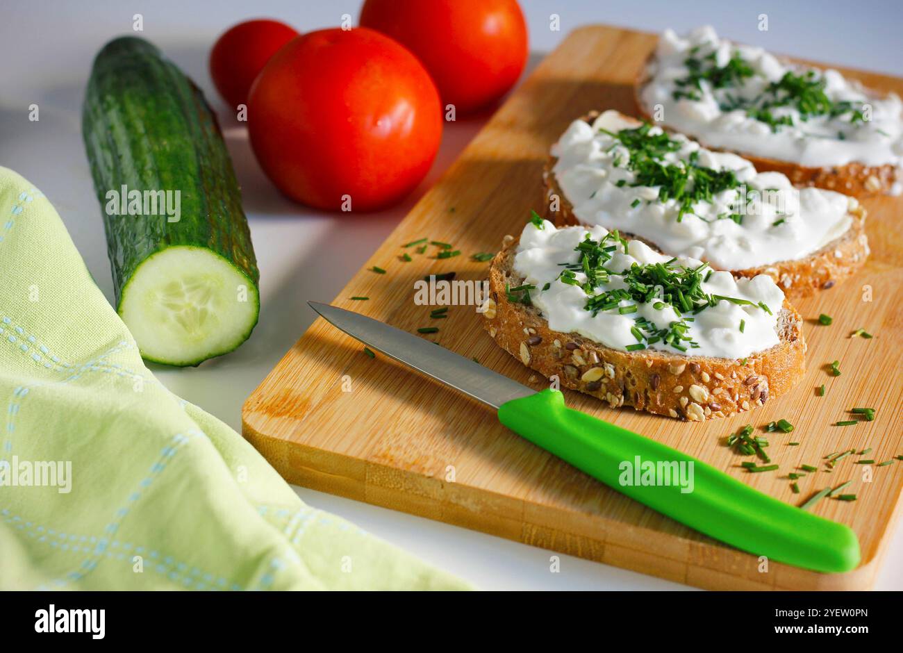 Gros plan de trois tranches de pain complet tartinées de beurre et de fromage cottage saupoudrées de ciboulette fraîchement hachée sur une planche à découper en bambou Banque D'Images