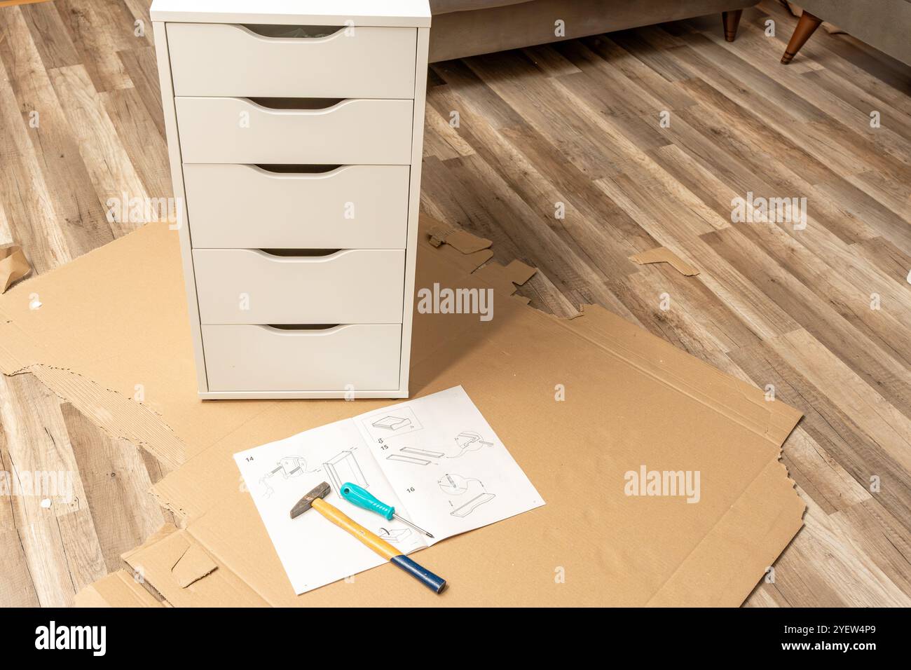 Un marteau et un tournevis reposent sur un morceau de papier avec des instructions pour assembler un meuble. A proximité, il y a une armoire déjà Assemblée Banque D'Images