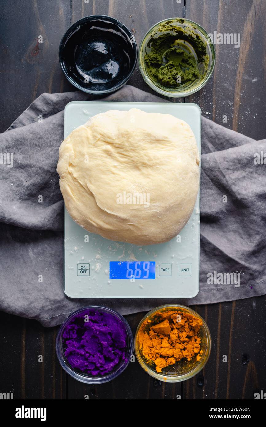 Pâte à pain sur une balance de cuisine avec colorants alimentaires naturels : faire du pain de lait multicolore avec du curcuma, du matcha, du charbon de bois et de la patate douce violette Banque D'Images