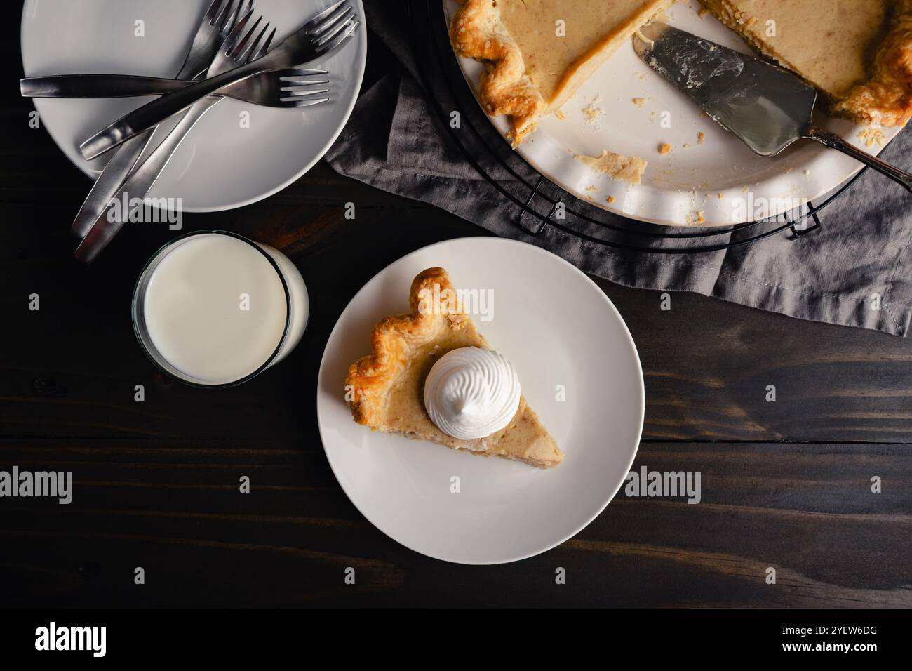 Vue aérienne de tranche de tarte à la citrouille blanche avec crème fouettée : tarte tranchée sur une assiette avec un verre de lait et fourchettes et assiettes supplémentaires sur le côté Banque D'Images