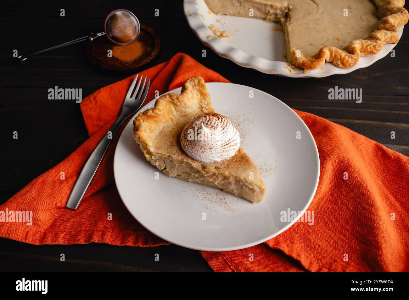 Vue latérale de tranche de tarte à la citrouille blanche avec crème fouettée : tarte tranchée sur une petite assiette avec un verre de lait et fourchettes et assiettes supplémentaires sur le côté Banque D'Images