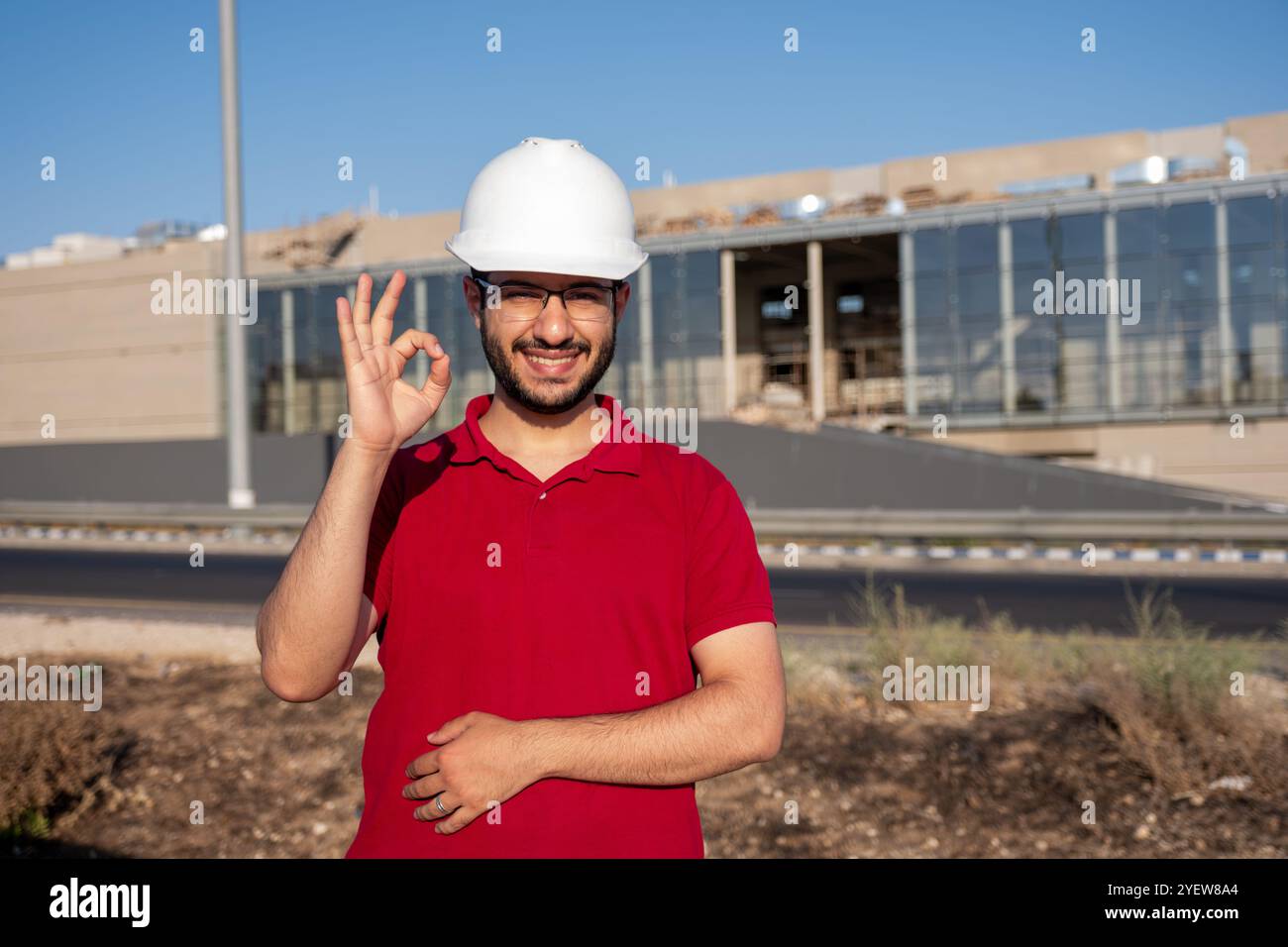 Un ingénieur en construction réfléchi portant un casque de sécurité se tient à l'extérieur, observant le chantier. Il réfléchit à l'avancement et au développement du projet Banque D'Images