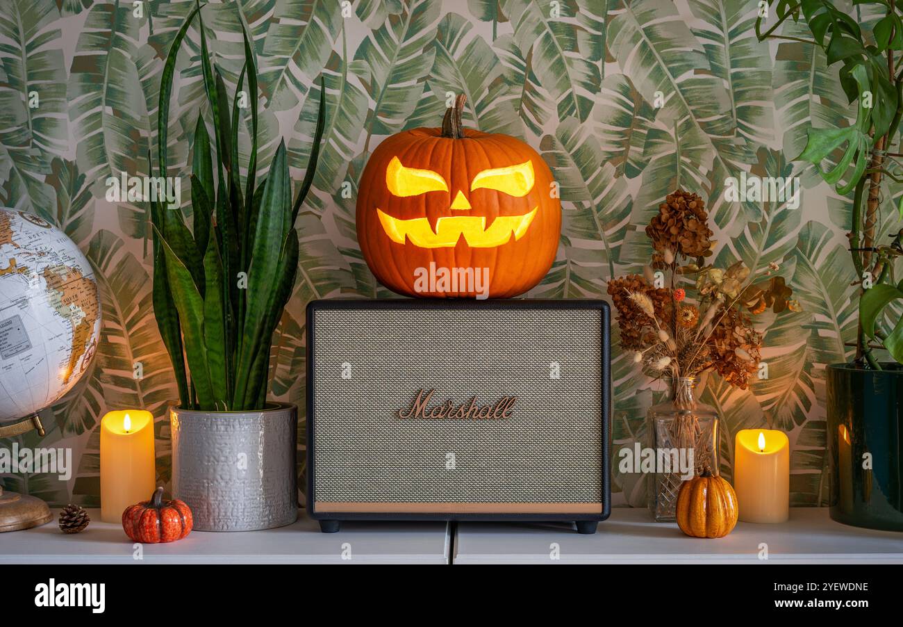 Enceinte bluetooth Marshall décorée dans un thème d'Halloween. Jack-o'-lanterne citrouille sculptée placée sur le haut-parleur entouré de bougies. Banque D'Images