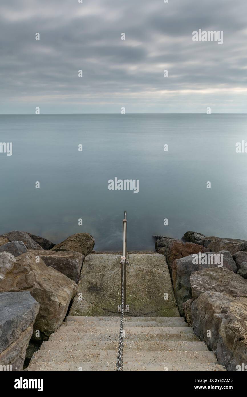 vol de marches de pierre ou d'escaliers menant à la mer sur le bord de mer avec des rochers de chaque côté dans un paysage marin dramatique atmosphérique ou sombre. Banque D'Images