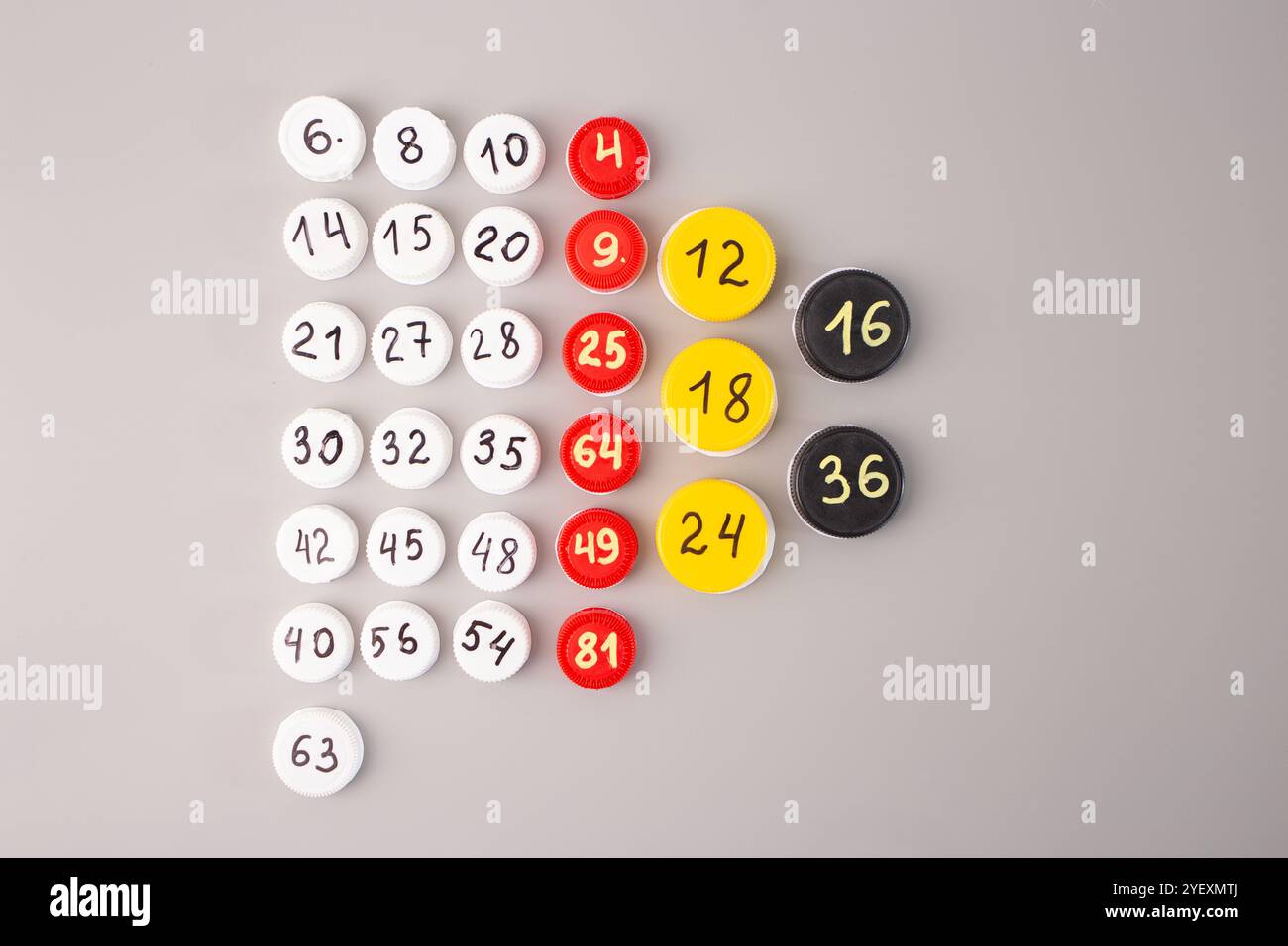 vue de dessus des bouchons de bouteilles en plastique avec des numéros écrits à la main pour les tables de multiplication disposées en rangées sur un fond gris. Outil d'apprentissage mathématique DIY pour Banque D'Images