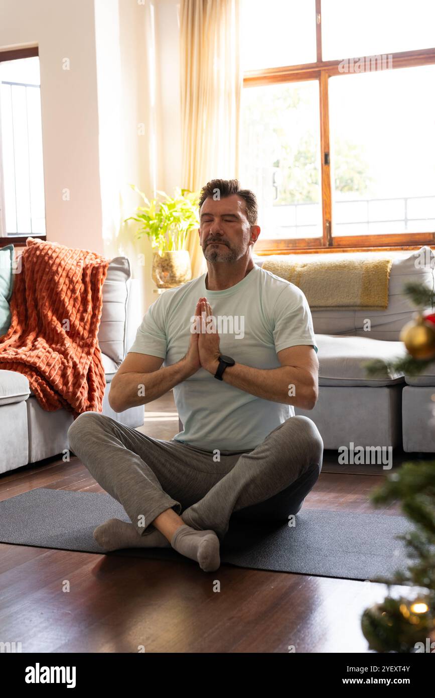 Homme senior méditant sur le tapis de yoga à la maison pendant la saison de Noël Banque D'Images