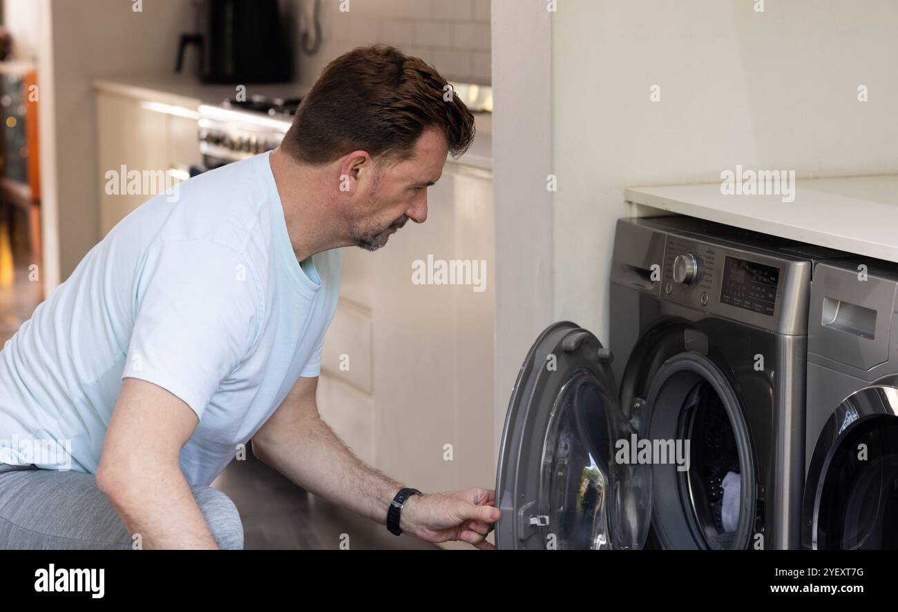 homme senior chargeant la machine à laver à la maison, en se concentrant sur les tâches ménagères Banque D'Images