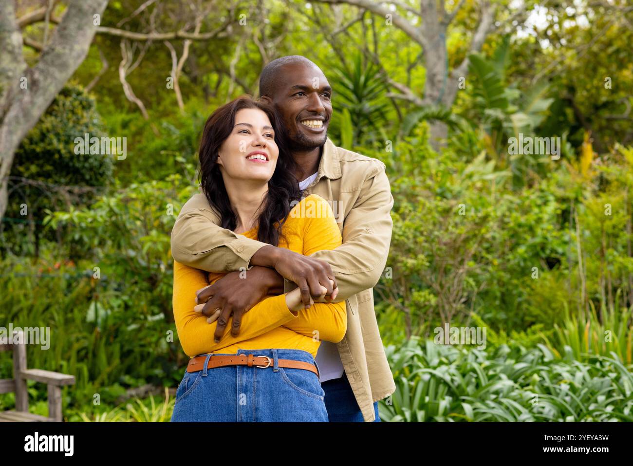 Couple multiracial souriant embrassant dans un jardin luxuriant, profitant d'un moment paisible en plein air ensemble Banque D'Images