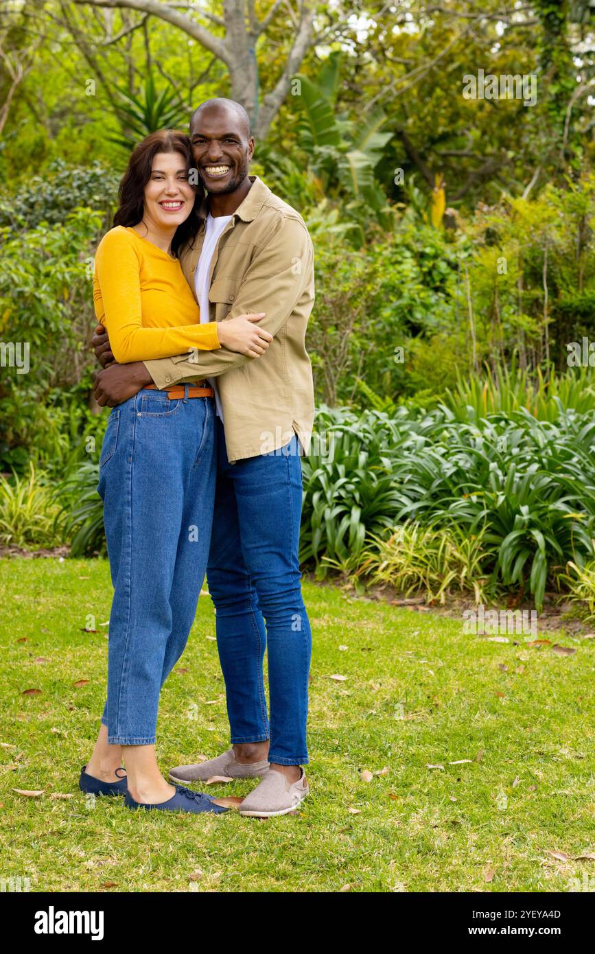 Couple multiracial souriant embrassant dans un jardin luxuriant, profitant d'une belle journée en plein air Banque D'Images