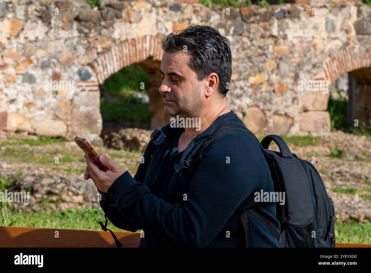 JEUNE HOMME ENVOYANT UN MESSAGE AVEC UN TÉLÉPHONE PORTABLE AVEC UN SAC À DOS NOIR Banque D'Images