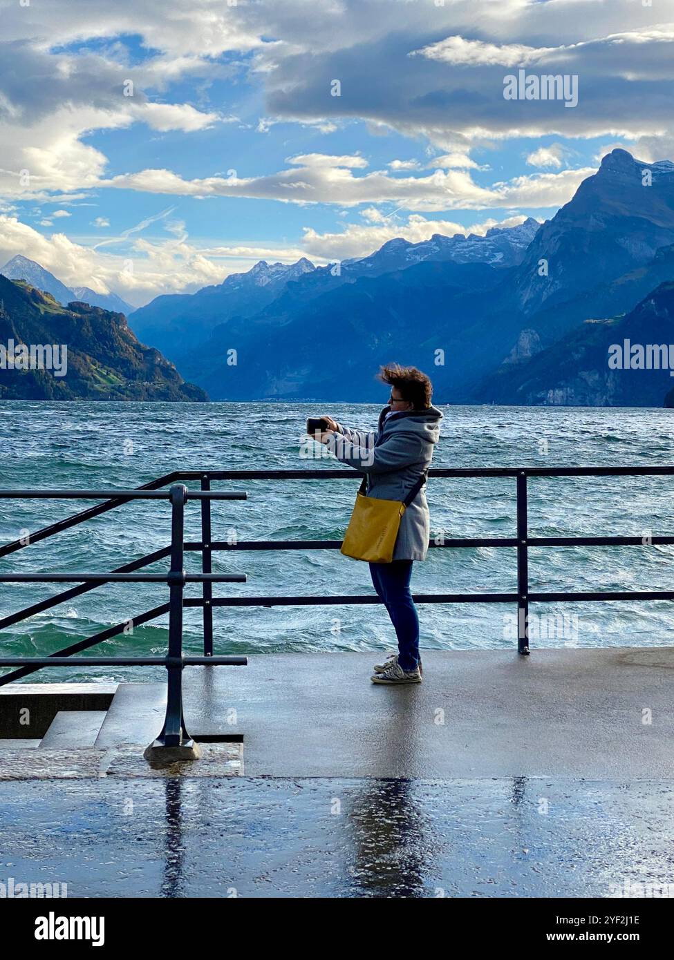 Femme prenant une photo avec un téléphone portable de pittoresque lac et montagne par une journée venteuse - Image de stock capturée avec un smartphone