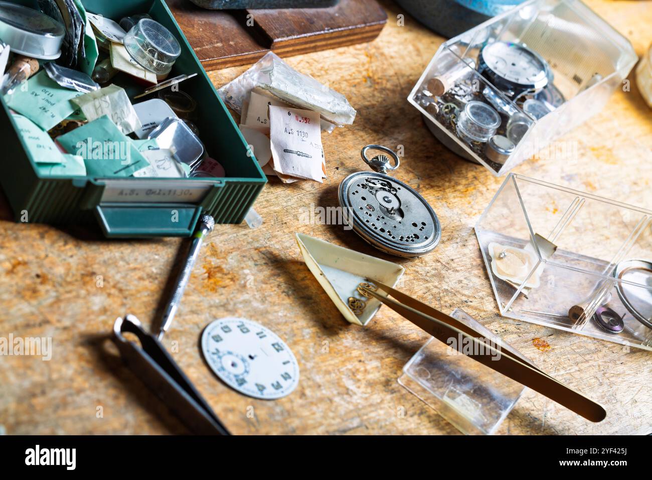 workspace contient des pièces de montres assorties, des pinces à épiler et des emballages étiquetés, représentant le chaos soigné et organisé inhérent à l'art de l'horlogerie Banque D'Images