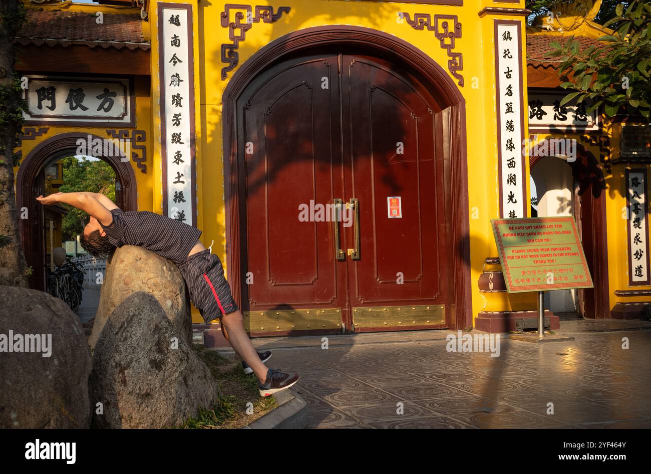 Un homme se penche en arrière sur un rocher pendant qu'il fait des exercices matinaux à l'extérieur de l'ancienne pagode Tran Quoc sur le lac de l'Ouest, Hanoi, Vietnam. Banque D'Images