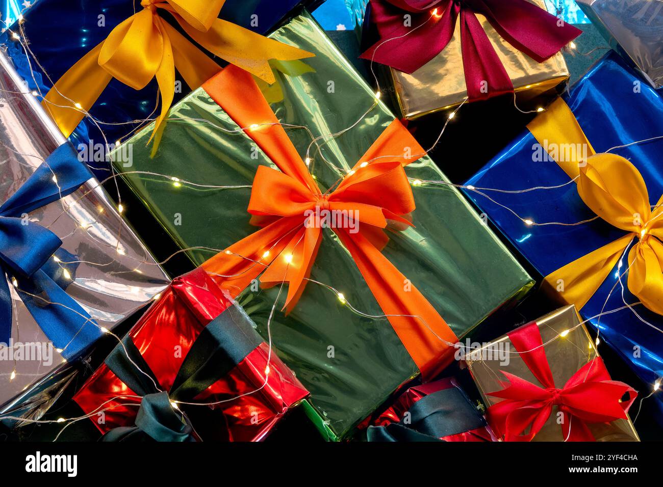 Un arrangement vibrant de boîtes-cadeaux emballées avec des rubans colorés et des guirlandes lumineuses scintillantes, créant un affichage festif et joyeux. Banque D'Images