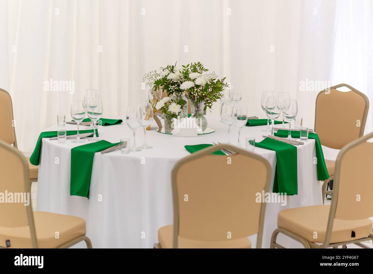 Verres à vin, vaisselle en argent et serviettes vertes sur des tables rondes recouvertes de nappe blanche. Concept de restauration. Intérieur de tente pour dîner de mariage, Banque D'Images