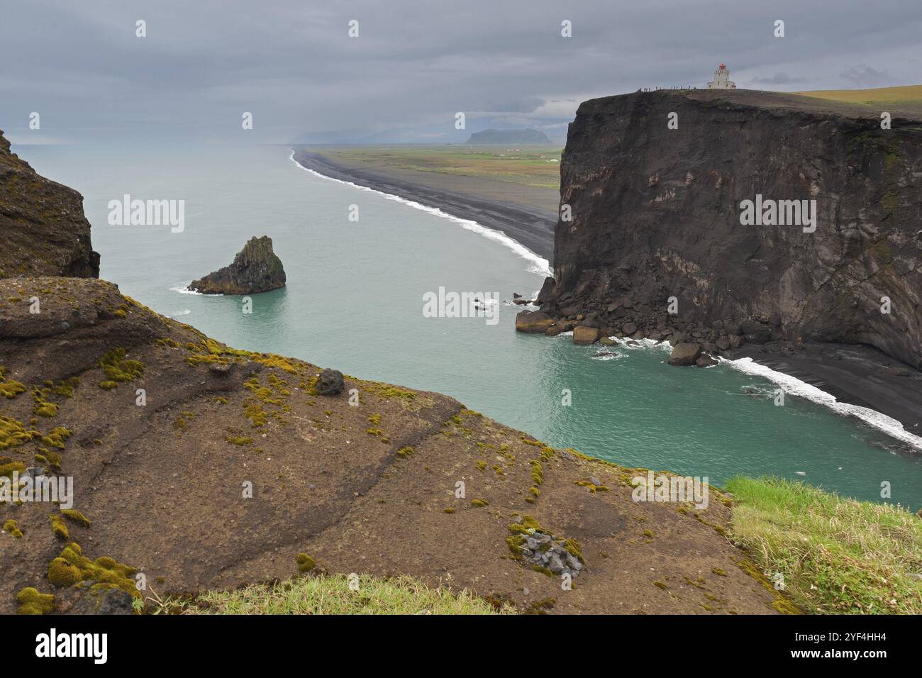 Falaises et côte avec mer, sous un ciel nuageux avec vue sur le phare, Dyrholafjara, porte rocheuse Dyrholaey ou Dyrholaey, côte sud, Islande, EUR Banque D'Images