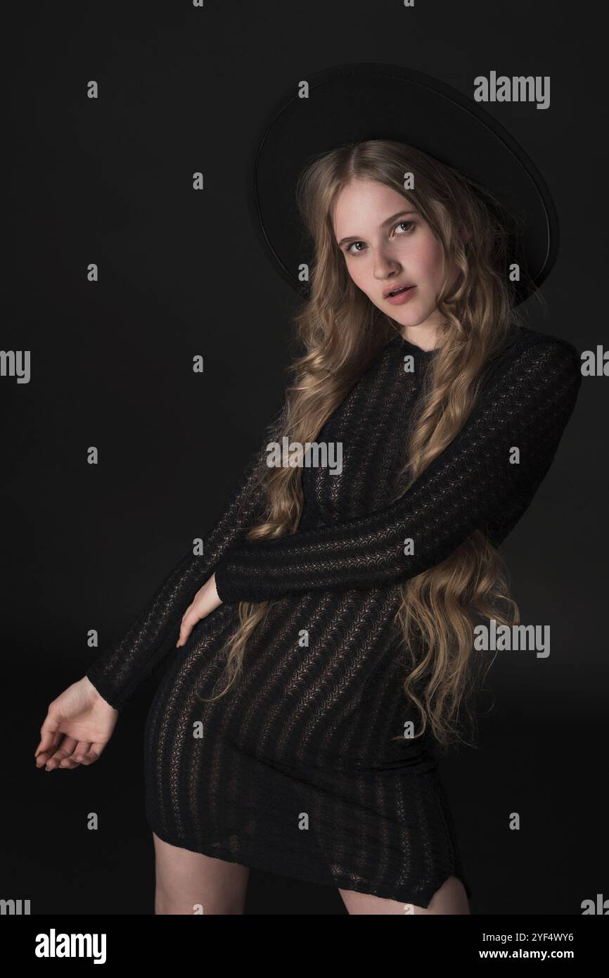 Portrait époustouflant d'un modèle blond élancé dégageant de la sensualité dans une pose détendue sur fond noir, regardant directement dans l'appareil photo. Le 2 Banque D'Images