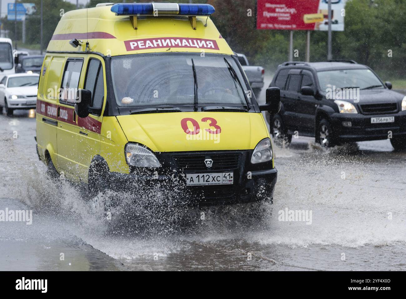 État urgence ambulance réanimation véhicule médical conduite pour aider le patient sur la route de la rue de la ville sur une flaque boueuse profonde, éclaboussant l'eau des roues. Banque D'Images