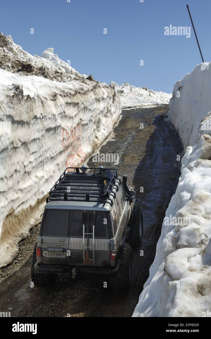 PÉNINSULE DU KAMCHATKA, EXTRÊME-ORIENT RUSSE, 18 JUIN 2017 : voitures hors route japonaises Toyota Land Cruiser Prado conduisant sur la route de montagne dans le tunnel de neige surroun Banque D'Images