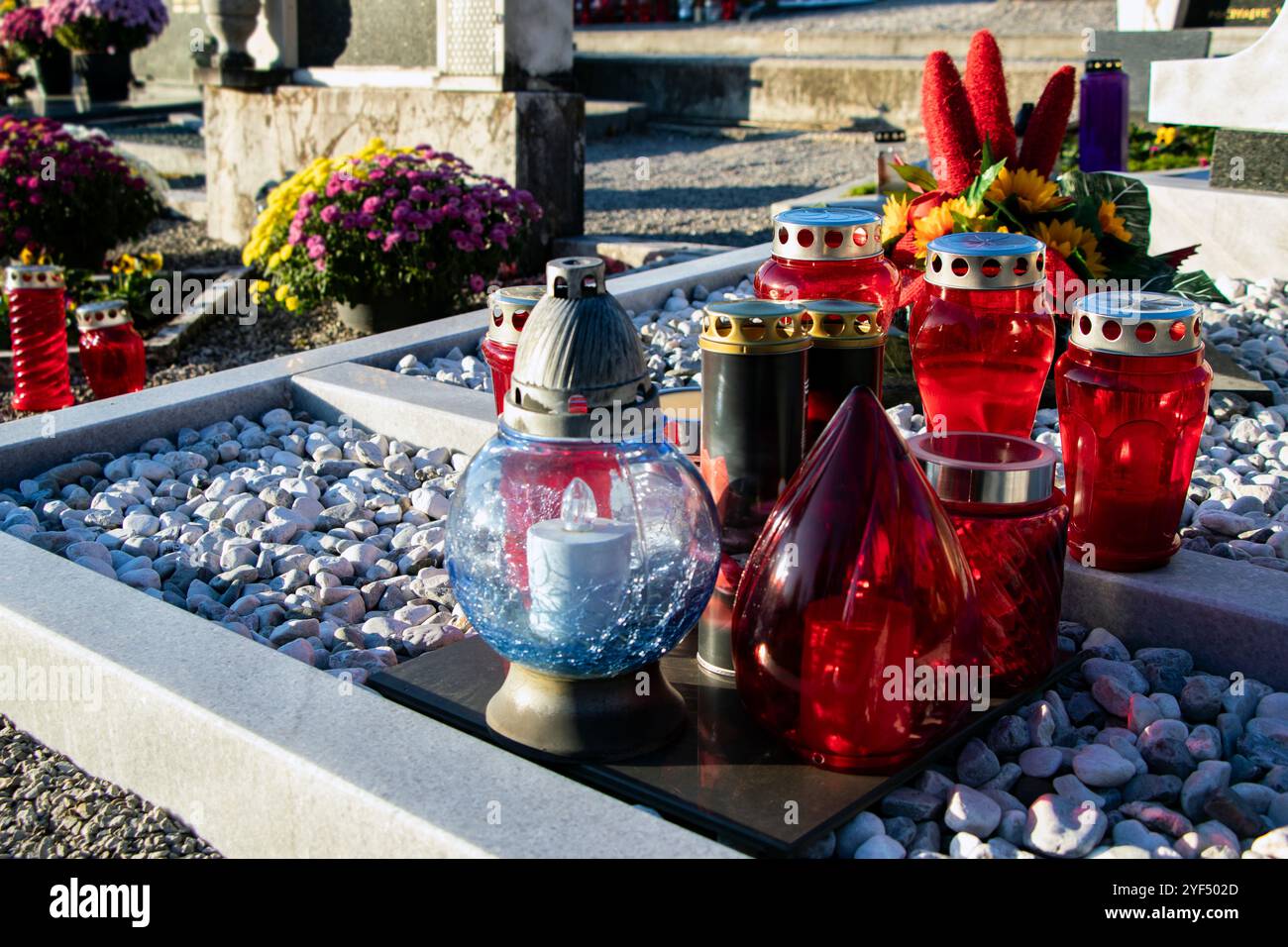 Tombe décorée de bougies rouges et bleues et de compositions florales vibrantes, symbolisant le souvenir et le respect. Banque D'Images