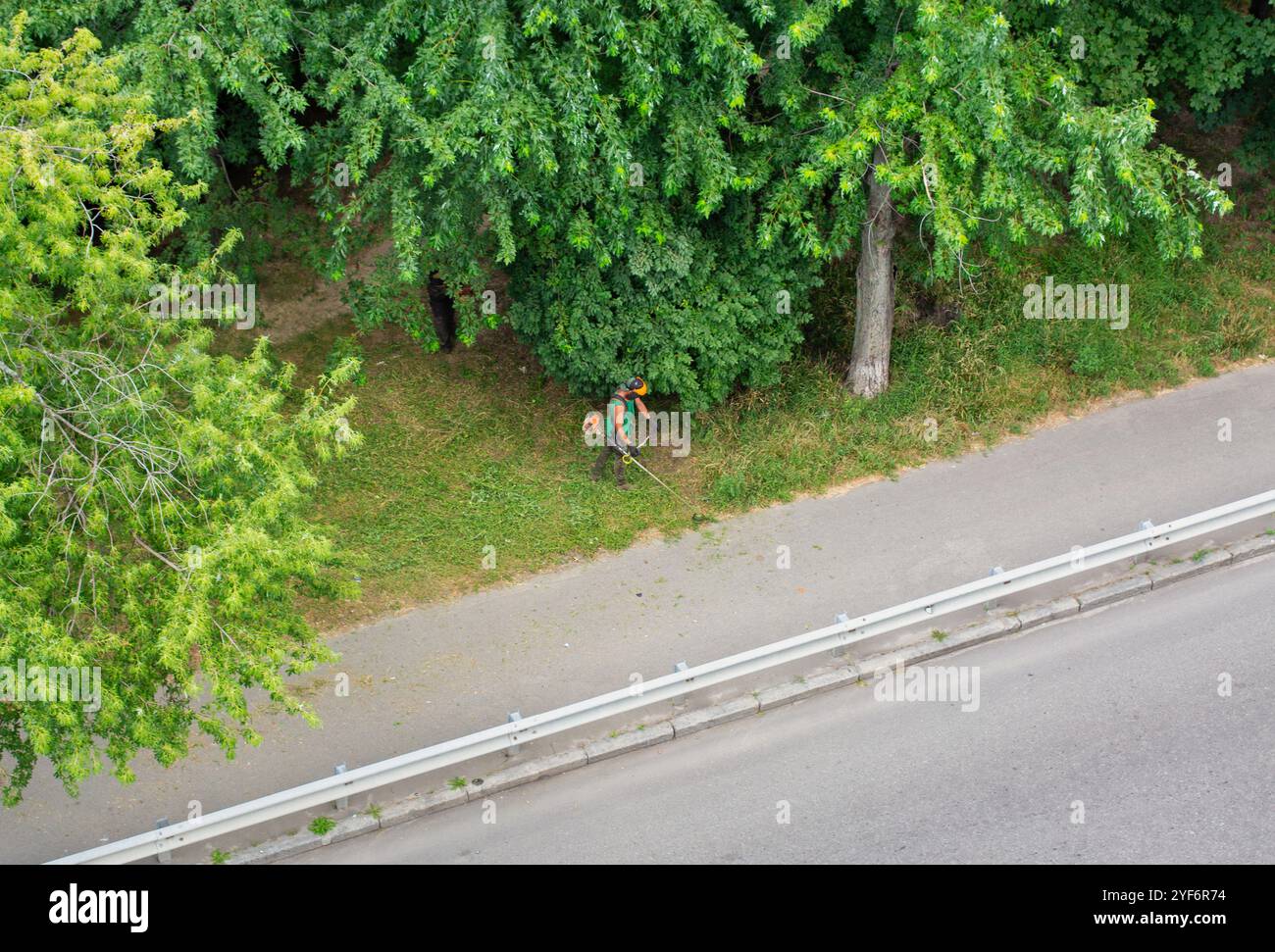 une équipe de travailleurs tond l'herbe avec un débroussailleuse à essence dans le parc de la ville, vue de dessus Banque D'Images