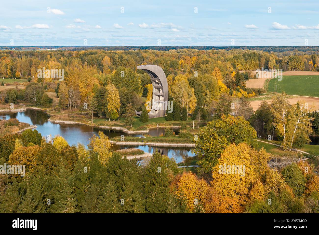 Une tour d'observation incurvée unique se dresse près d'un plan d'eau calme, entouré de feuillage d'automne doré, orange et vert dans un paysage rural. Banque D'Images