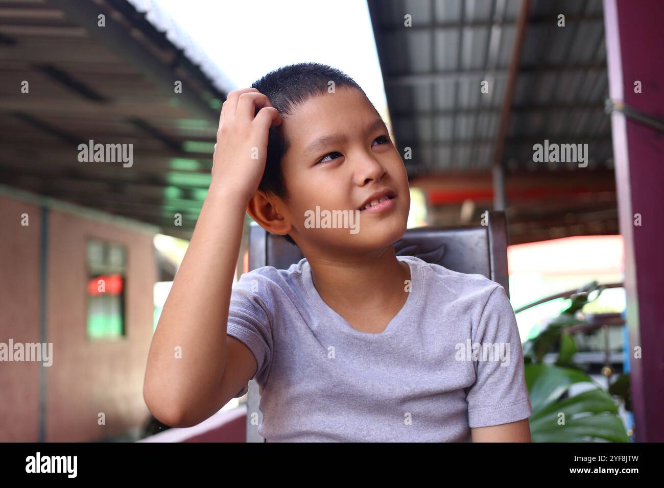 Un jeune garçon réfléchi est assis à l'extérieur dans une chemise grise décontractée, réfléchissant sur la vie. Son expression exprime un sentiment d’innocence et de curiosité. Parfait fo Banque D'Images